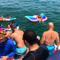 Adults and children playing in the water behind our Miami boat charter.